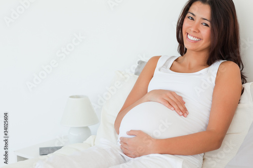 Photo: Beautiful pregnant woman posing while lying on a bed Beautiful pregnant woman posing while lying on a bed