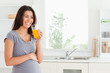 Good looking pregnant woman drinking a glass of orange juice whi