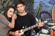 a woman and a guitarist in front of a tagged wall