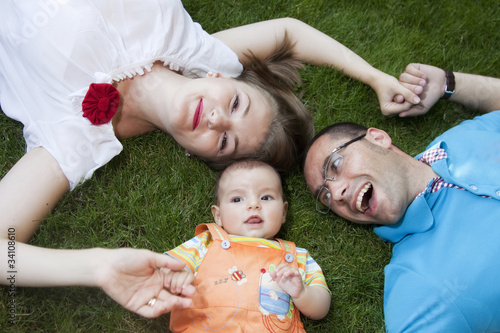 Photo: Happy family with baby boy laying in grass Happy family with baby boy laying in grass