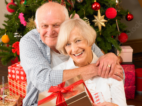 Photo: Senior couple with gifts in front of Christmas tree Senior couple with gifts in front of Christmas tree