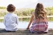 Rear view of siblings sitting together at a pier