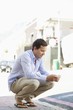 Man crouching and text messaging on a mobile phone