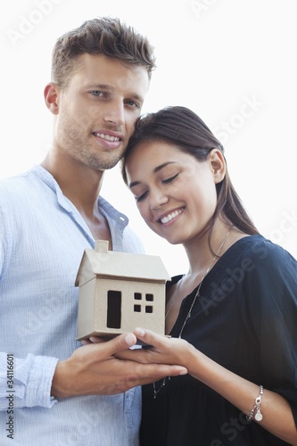 Photo: Cute young couple holding small model house Cute young couple holding small model house