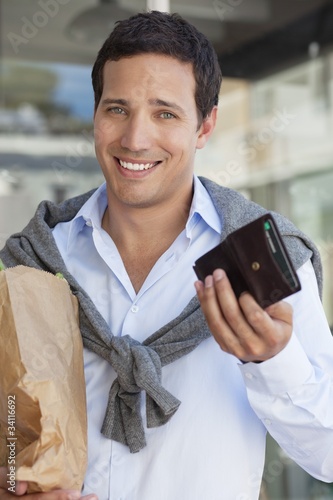 Photo: Portrait of a man showing empty wallet with paper bag full of vegetables Portrait of a man showing empty wallet with paper bag full of vegetables