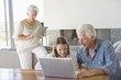 Man using a laptop with his granddaughter and his wife working on a digital tablet in background