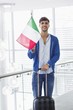 Portrait of a man holding Italian flag and a suitcase at an airport
