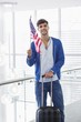 Portrait of a man holding American flag and a suitcase at an airport