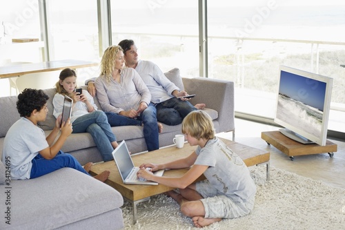 Photo: Couple watching television set while their children busy in different activities Couple watching television set while their children busy in different activities