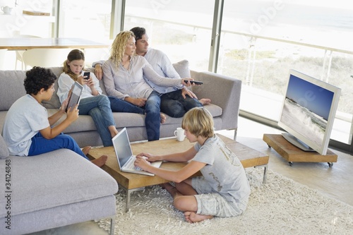 Photo: Couple watching television set while their children busy in different activities Couple watching television set while their children busy in different activities