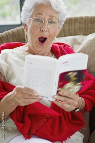Photo: Senior woman reading a magazine and looking surprised Senior woman reading a magazine and looking surprised
