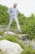 Senior man jumping over rocks in a garden