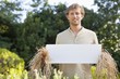 Young man in scarecrow dressing and holding a blank placard in a field