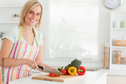 Photo: Cute woman cutting red pepper looks into camera Cute woman cutting red pepper looks into camera