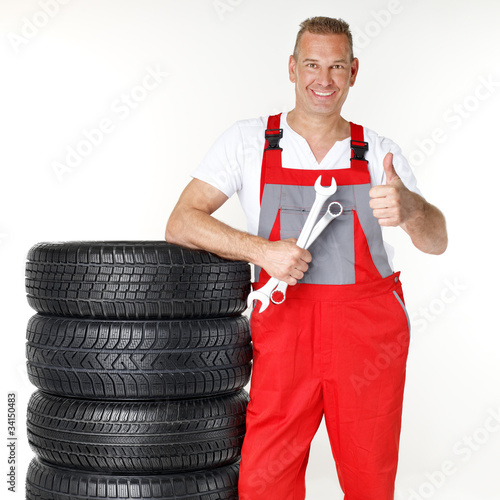 Foto: Motor mechanic next to a set of winter tyres shows thumb up Motor mechanic next to a set of winter tyres shows thumb up