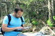 Young man with backpack looking at map in the woods