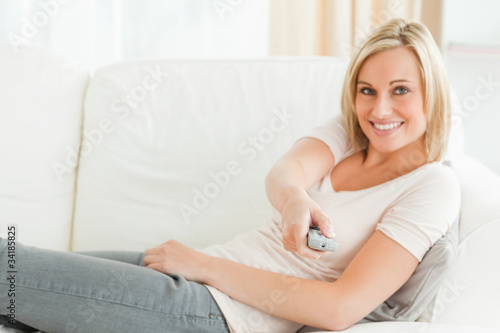 Photo: Woman pointing a remote at the camera with a knowing smile Woman pointing a remote at the camera with a knowing smile