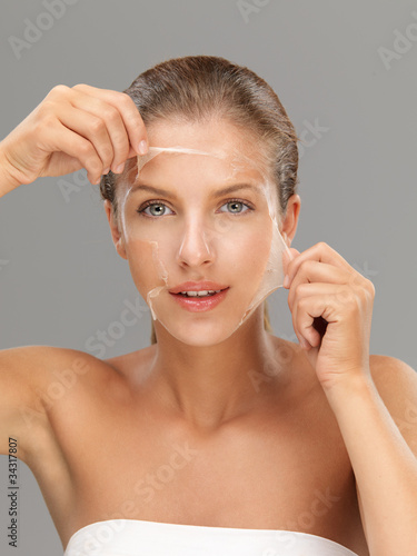 Photo: young woman taking off peeling mask young woman taking off peeling mask