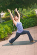 woman doing yoga posture warrior 1 outdoors in public on mat