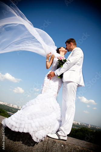 Photo: newly married couple kissing.wind lifting white bridal veil newly married couple kissing.wind lifting white bridal veil
