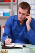 Man in overalls with a phone and ringbound organizer