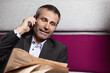 Businessman chatting on mobile phone and reading newspaper.