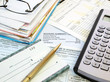 A pile of bills, checkbook, pen and calculator on the table.