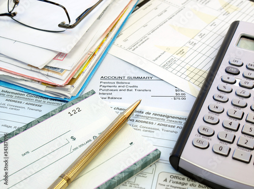 Photo: A pile of bills, checkbook, pen and calculator on the table. A pile of bills, checkbook, pen and calculator on the table.