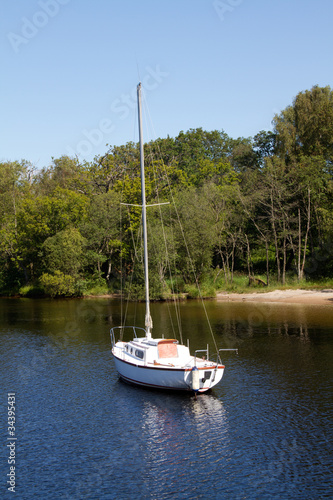Foto: A small yacht is is anchored in the water beside an island A small yacht is is anchored in the water beside an island