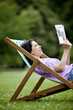 A young woman sitting on a deckchair, looking at a guidebook