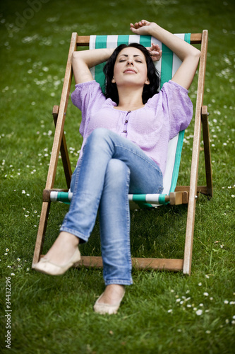Photo: A young woman sitting on a deckchair, enjoying the sunshine A young woman sitting on a deckchair, enjoying the sunshine