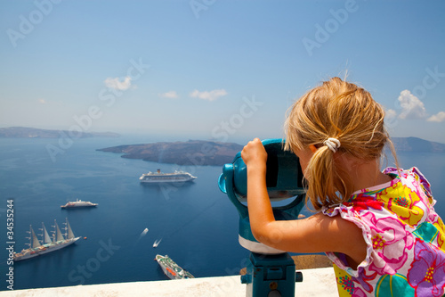 Photo: Girl looking with binoculars in Thira, Santorini, Greece Girl looking with binoculars in Thira, Santorini, Greece