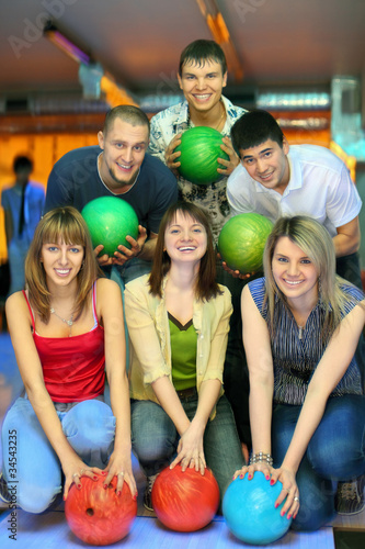 Photo: Girls of squatting and fellows back stand with ball for bowling Girls of squatting and fellows back stand with ball for bowling