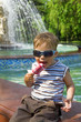 boy in sun glasses eats ice-cream against a fountain boy in sun glasses eats ice-cream against a fountain