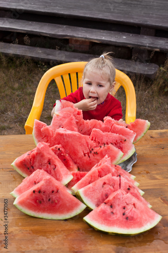 Photo: Little child eating watermelon. Many red slices on table Little child eating watermelon. Many red slices on table