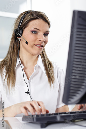 Foto: young beautiful woman with headset and computer in office young beautiful woman with headset and computer in office