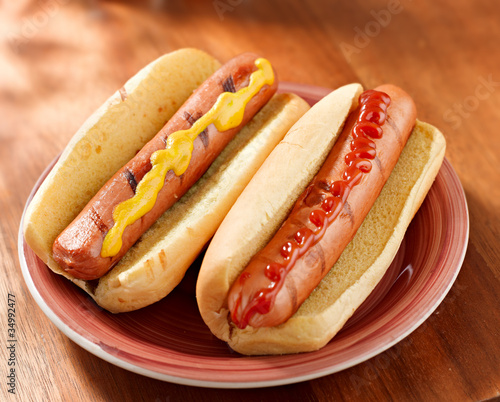 Photo: two hotdogs on a plate with ketchup and mustard. two hotdogs on a plate with ketchup and mustard.