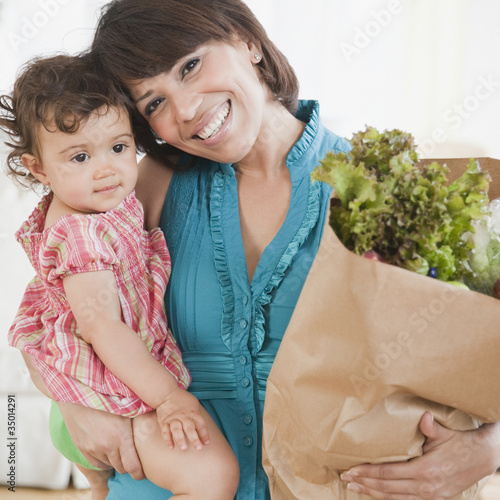 Photo: Hispanic woman carrying daughter and groceries Hispanic woman carrying daughter and groceries