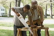 African grandfather watching grandson saw wood