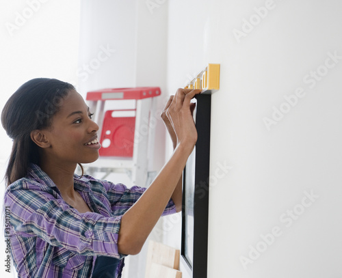 Foto: Mixed race woman hanging picture Mixed race woman hanging picture