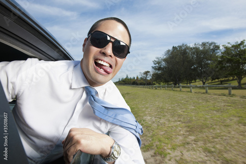 Photo: Asian businessman riding in car with head out window Asian businessman riding in car with head out window