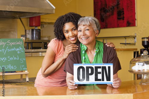 Photo: African American business owners in cafe holding open sign African American business owners in cafe holding open sign