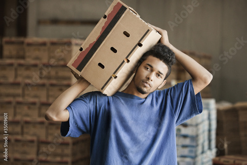 Photo: Mixed race man carrying cardboard box in warehouse Mixed race man carrying cardboard box in warehouse