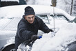 Hispanic man removing snow from car