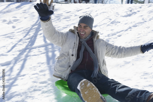 Photo: Mixed race man sledding on hill Mixed race man sledding on hill