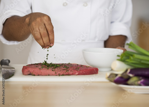 Photo: Mixed race chef seasoning steak Mixed race chef seasoning steak