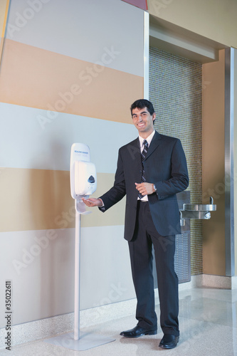 Photo: Hispanic businessman using hand sanitizer in lobby Hispanic businessman using hand sanitizer in lobby