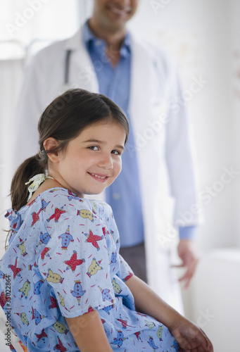 Photo: Smiling mixed race girl in examination room with doctor in background Smiling mixed race girl in examination room with doctor in background