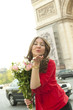 Caucasian woman holding bouquet and blowing kisses near Arc de Triomphe