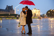 Caucasian couple kissing in rain at night near the Louvre